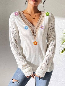 Detail of V-neck lace patchwork with colorful 3D knitted flowers on white sweater