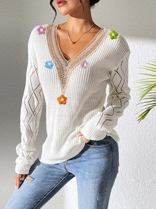 Close-up of white knit sweater featuring colorful 3D crochet flowers and lace V-neck detail