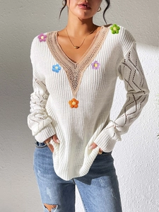 Detail of white knit sweater featuring handmade colorful crochet flowers and V-neck lace