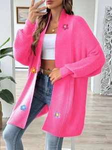 Détail d'un cardigan en maille rose vif avec des fleurs au crochet faites à la main