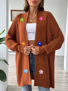 Détail d'un cardigan en maille caramel avec des patchs de fleurs colorées au crochet