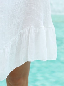 Gros plan sur l'ourlet à volants d'une robe de plage blanche sur fond d'eau bleue