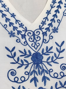 Détail de broderies bleues sur robe de plage blanche à col en V de style bohème chic