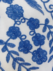 Gros plan d'une broderie florale bleue sur une robe de plage blanche avec détails fins