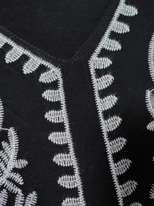 Detailed view of white leaf embroidery on a black V-neck bohemian beach dress