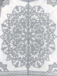 Detailed macro view of white floral lace fabric with grey mandala embroidery and wavy edge