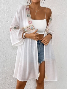 Vista dettagliata del kimono in pizzo bianco con ricami etnici colorati e nappe eleganti