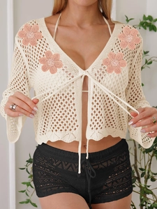 Dettaglio della trama all'uncinetto e ricami floreali rosa sul cardigan beige
