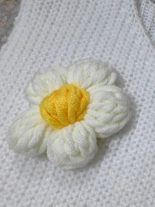 Close-up of handmade crochet white and yellow floral appliqué detail on knitwear cardigan
