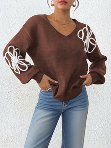 Close-up of white floral ribbon embroidery on a deep brown V-neck knit sweater
