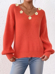 Detail eines orangefarbenen V-Ausschnitt-Pullovers mit handgefertigten Gänseblümchen