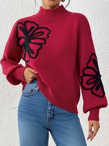 Detailed view of black floral embroidery and lantern sleeves on a red knit sweater