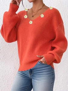 Detail weißer Gänseblümchen-Applikationen auf dem korallenfarbenen Strickpullover