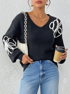Detail of 3D white floral embroidery on a black V-neck long sleeve knit sweater