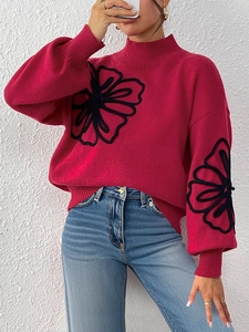Detailed view of black floral embroidery and ribbon stitching on a red high-neck sweater
