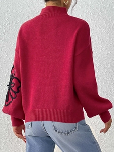 Detail view of red lantern sleeves and black floral embroidery on a knit sweater