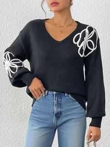 Detail view of large white floral embroidery on a black V-neck knitted sweater for women
