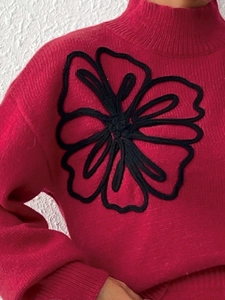 Close-up of rose red knit sweater featuring black floral embroidery and mock neck detail