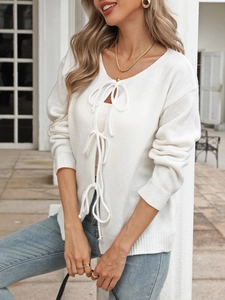 Detail of white knit cardigan featuring front ribbon bow closures and ribbed sleeve cuffs
