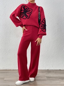 Close-up of red knit sweater featuring black floral embroidery and matching wide-leg pants