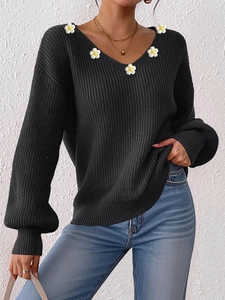 Detail eines schwarzen Strickpullovers mit V-Ausschnitt, Häkelblumen und Puffärmeln