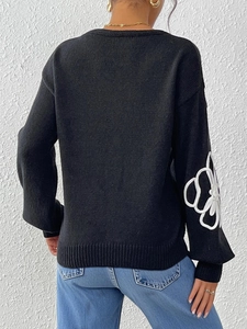 Back view of black knit sweater featuring white floral embroidery and ribbed edges