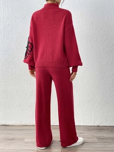 Detail of red knit sweater sleeve showing delicate black floral ribbon embroidery