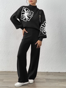Detailed embroidery of white floral patches on black knitted sweater and wide-leg trousers