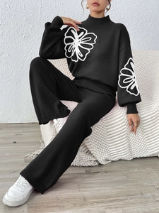 Detail of black knit sweater with white crochet flower embroidery and ribbed texture