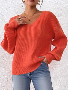 Dettaglio del maglione a trecce arancione con scollo a V e polsini a costine fini