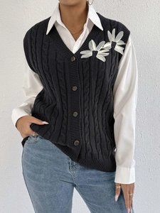 Detail of cable knit vest featuring 3D floral appliques and dark buttons on front