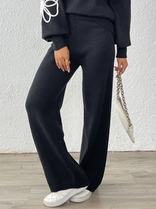 Dettaglio dei pantaloni larghi in maglia nera e manica con ricamo a fiori bianchi