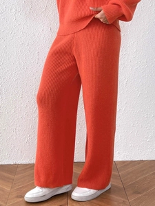Detail of orange knitted wide-leg trousers showing vertical ribbed texture and fabric drape