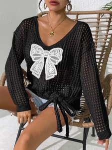 Detail der hohlen Stricktextur mit weißer Spitzenschleife und Kordelzug am schwarzen Pullover