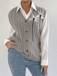 Detail of cable knit vest with 3D floral accents and long tassels over a white shirt