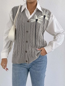 Detail of grey cable knit vest with white 3D flower appliques and brown buttons