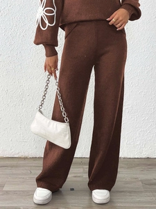 Dettaglio dei pantaloni larghi in maglia caffè scuro con motivo floreale sulle maniche