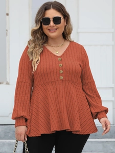 Detail of the V-neckline with decorative gold buttons on a ribbed knit brick red top