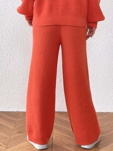 Detail of orange knitted wide-leg trousers and sweater showing vertical ribbed texture