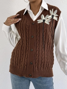 Detail of cable knit vest featuring 3D white flower applique and decorative black ribbons