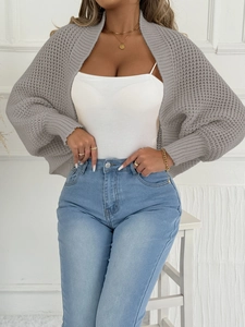 Detail eines grauen Strick-Cardigans mit weißem Neckholder-Top und blauer High-Waist-Jeans