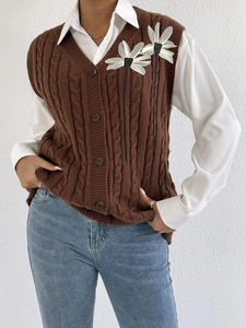 Detail of brown cable-knit vest with V-neck, buttons, and white mesh flower embroidery