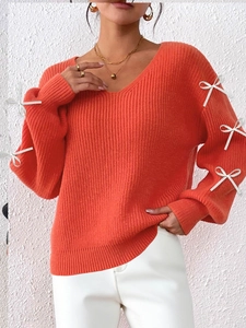 Detail of bright orange V-neck knit sweater featuring ribbed texture and stylish ribbon