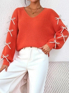 Detailed view of orange knit sweater featuring white ribbon bows on long sleeves