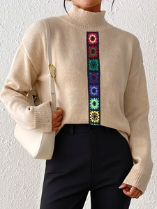 Detail of colorful crochet flower patches on a beige high-neck knitted pullover sweater