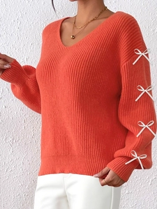 Detailed close-up of orange V-neck knit sweater with white ribbon bows on the sleeves