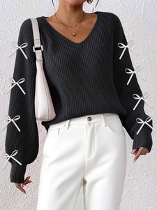 Detail of elegant V-neck sweater featuring chic white bow tie accents on the sleeves