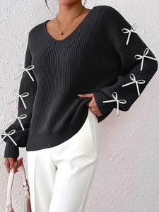Close-up of black V-neck knit sweater with white ribbon bows on long sleeves