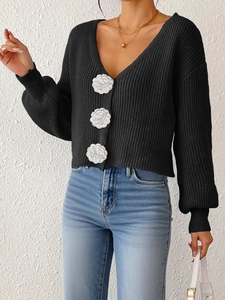 Close-up of black knit cardigan featuring three large white camellia flower buttons