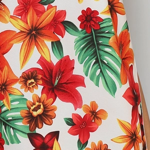 Close-up detail of tropical floral print on white fabric with red lilies and green leaves